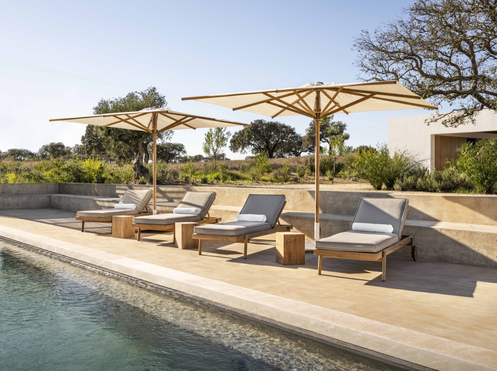 Contract-grade poolside loungers and a wood-framed parasol on a luxury infinity-pool deck